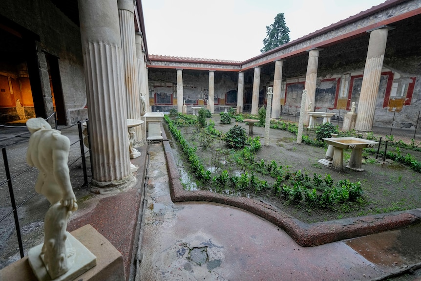 A roman courtyard with rows of columns and plants lining the middle. 