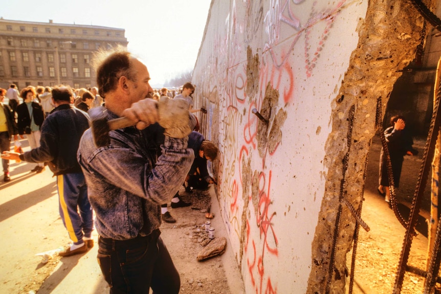 Man aiming hammer at Berlin Wall between Brandenburg Gate and Reichstag in November 1989.