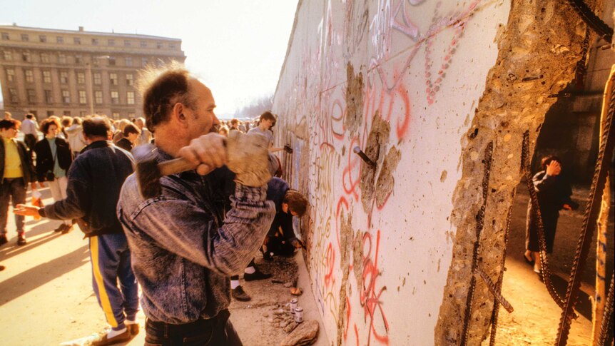 Man aiming hammer at Berlin Wall between Brandenburg Gate and Reichstag in November 1989.