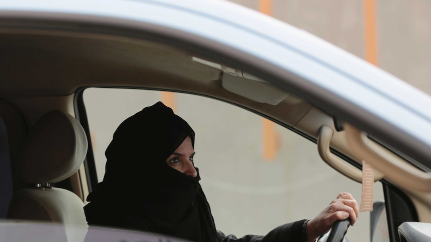 A woman in a black hijab sits behind the wheel of a car in Saudi Arabia.