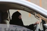 A woman in a black hijab sits behind the wheel of a car in Saudi Arabia.