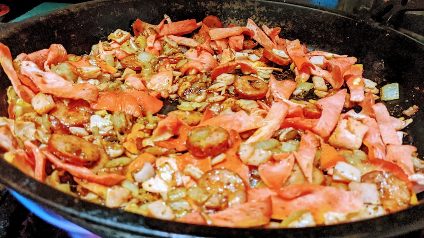 a mixture of pink oyster mushrooms, chorizo and rice cooking in a frying pan. 