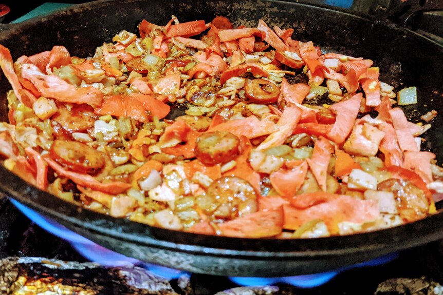 a mixture of pink oyster mushrooms, chorizo and rice cooking in a frying pan. 