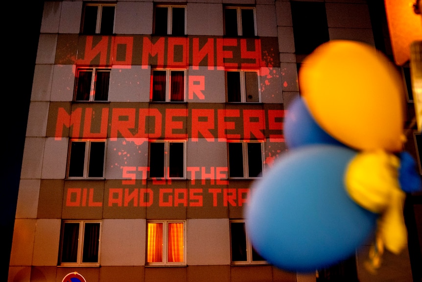 The words "No Money for Murderers, Stop the Oil and Gas Trade" are projected onto the wall of the Russian consulate in Germany. 