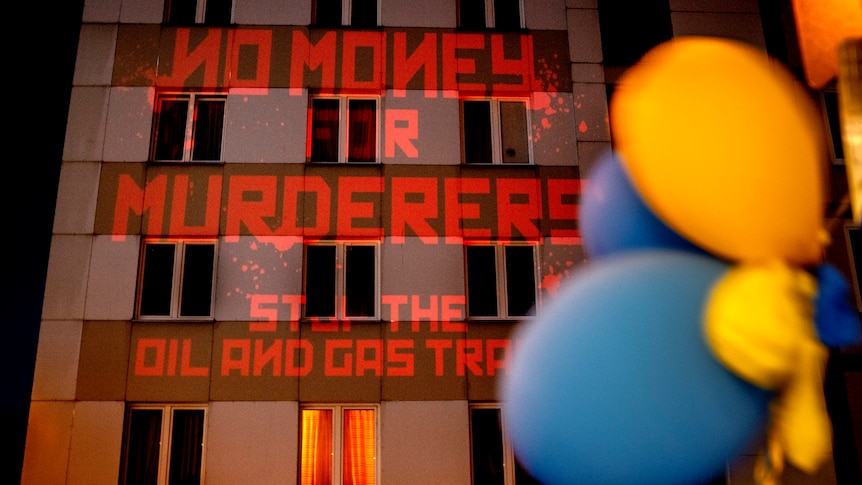 The words "No Money for Murderers, Stop the Oil and Gas Trade" are projected onto the wall of the Russian consulate in Germany. 