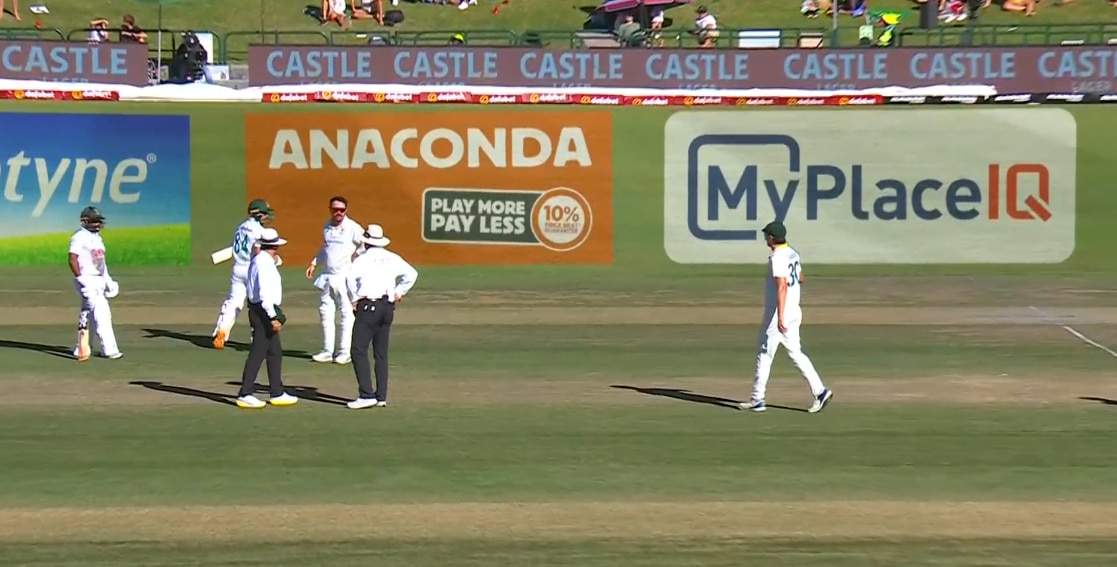 Three cricketers and two umpires in discussion on the pitch
