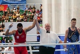 A referee holds up a man's hand in victory, while another man stands on the other side.