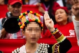 A woman in colourful traditional Kachin dress gives a three-finger salute. Her face is blurred.