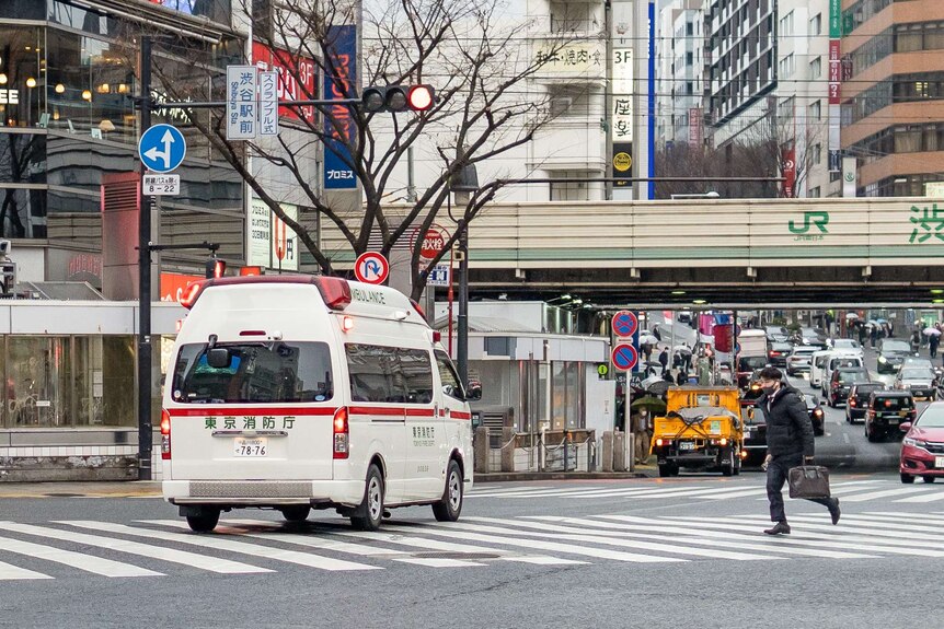 An ambulance drives by on a Tokyo street as a man runs with a briefcase.