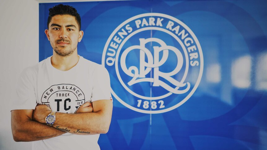 Massimo Luongo standing in front of a QPR sign.