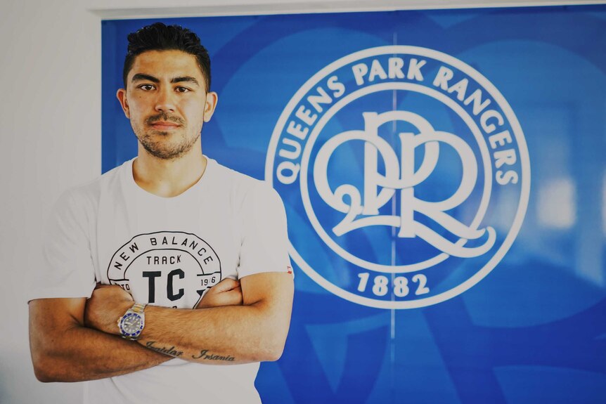 Massimo Luongo standing in front of a QPR sign.