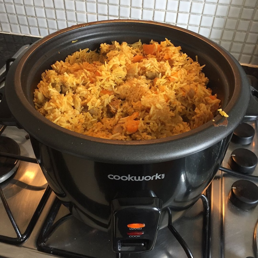 A basic rice cooker filled with biryani - yellow rice with bits of carrot and chicken.