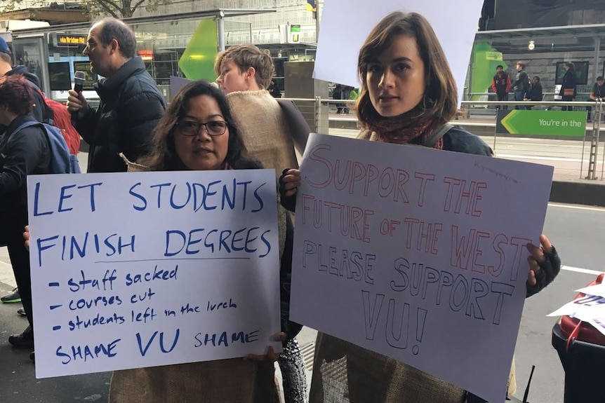 Two women hold signs saying "Let students finish degrees" and "Support the future of the west".