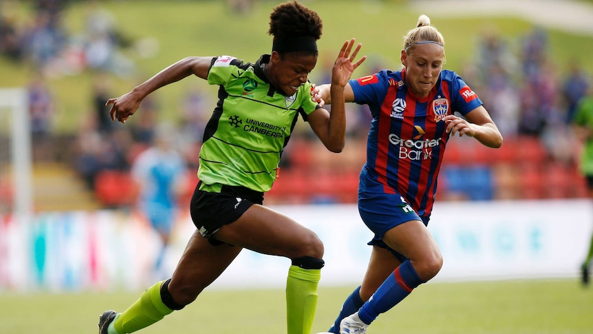 A W-League attacker runs with the ball down the wing as a defender tries to cut in on her.