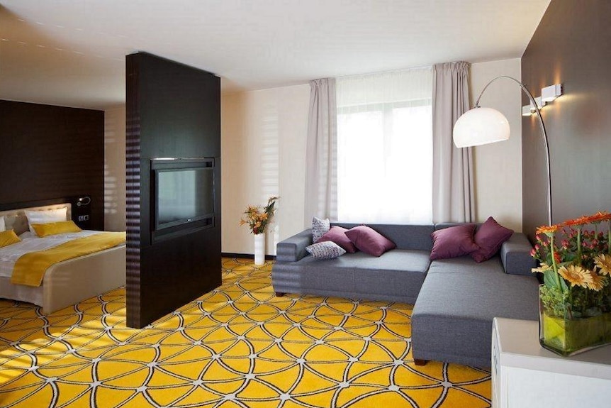 A hotel room that has a lounge, tv and large bed inside it. The carpet is a bright yellow design.