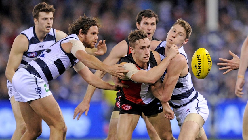 Luke Dunstan of the Saints passes the ball as he's tackled by Mark Blicavs and Steven Motlop of the Cats