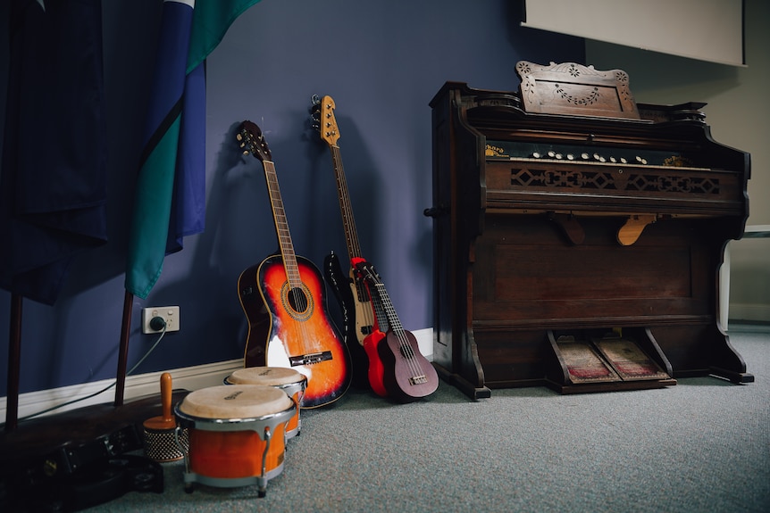 A few guitars and drums sit on a carpeted floor next to a piano.