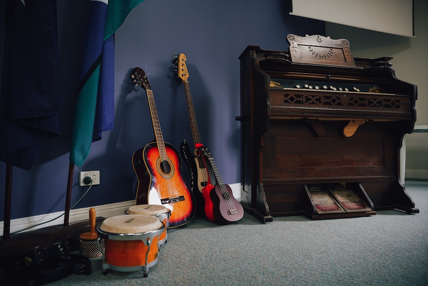 Quelques guitares et percussions sont posées sur une moquette à côté d'un piano.