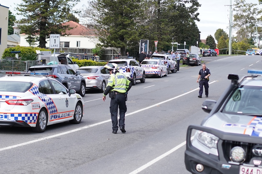 Many police cars line a street as officers walk around. 