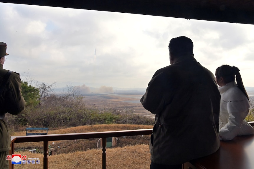 Kim Jong-un se tient avec sa fille derrière une balustrade, regardant un lancement de missile dans le ciel.