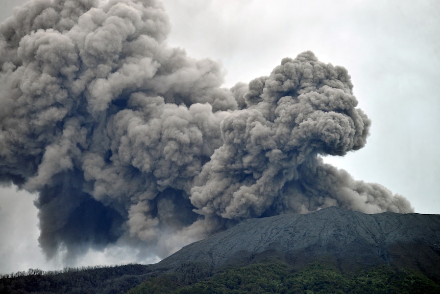 Mount Marapi volcano spews a huge thick grey cloud of volcanic ash into a grey sky.