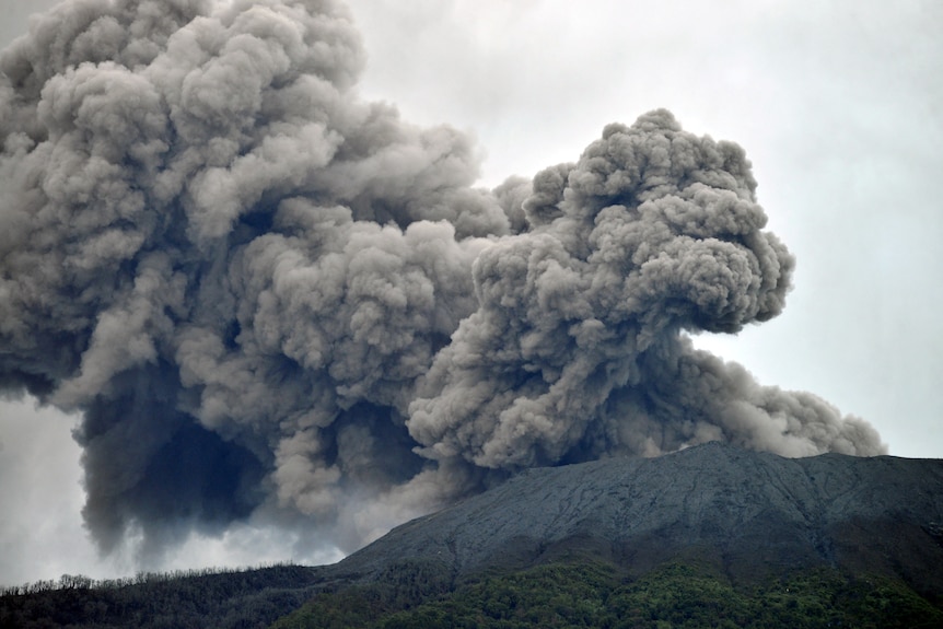 El volcán Monte Marapi arroja una enorme y espesa nube gris de ceniza volcánica hacia un cielo gris.