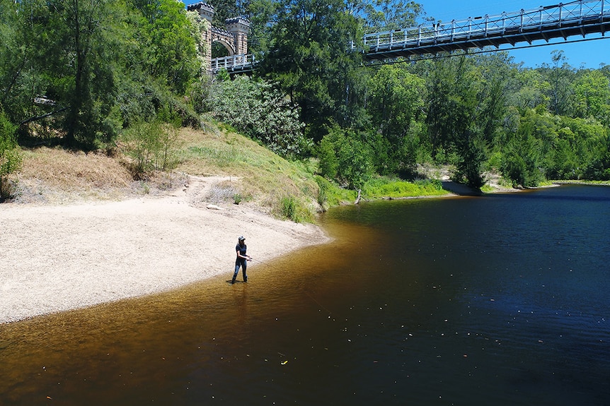 Erin Lake stands on the banks of the Kangaroo Valley River fishing under the Hampden Bridge.