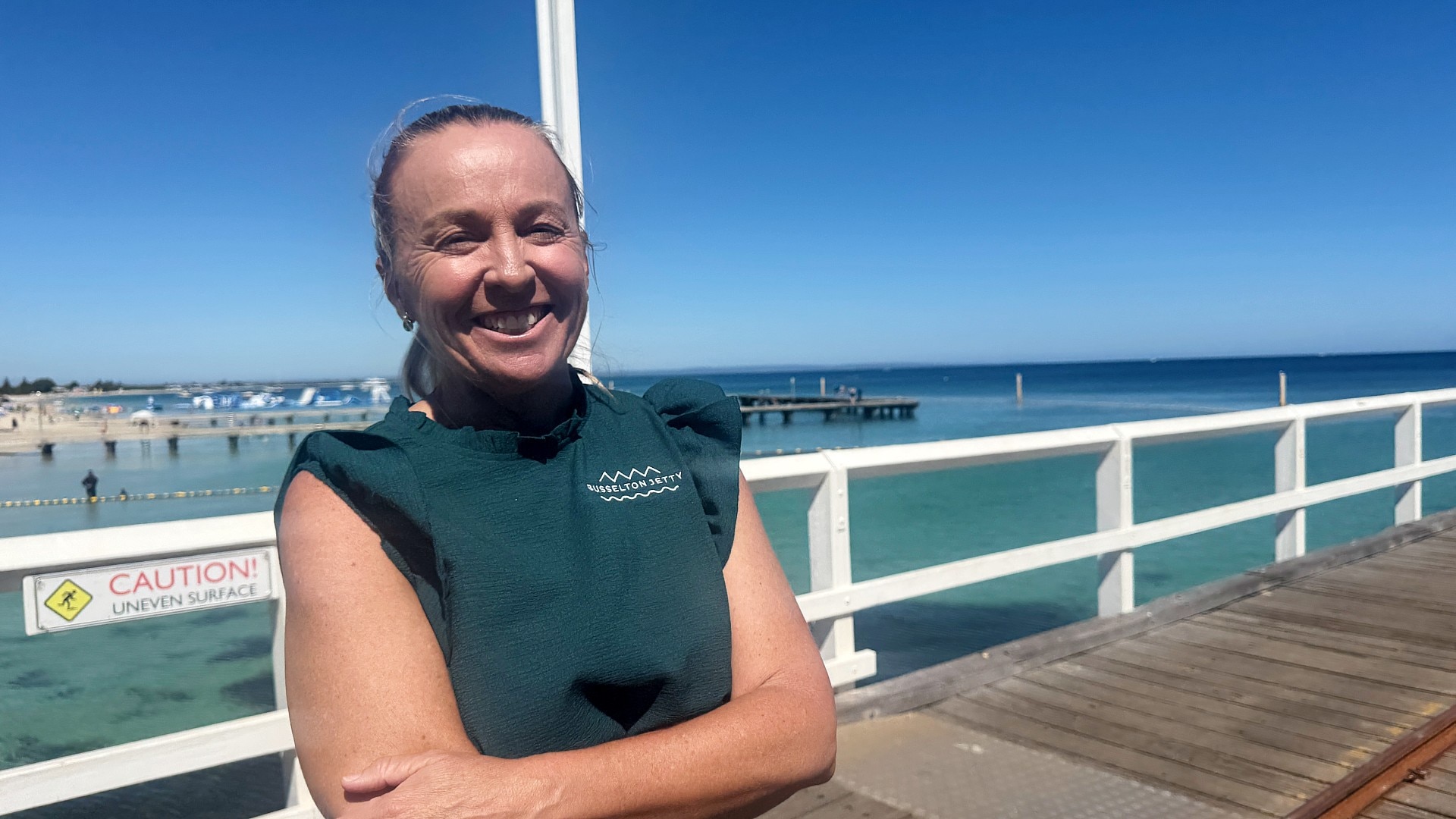 Uma mulher de camisa verde está no cais de Busselton. 
