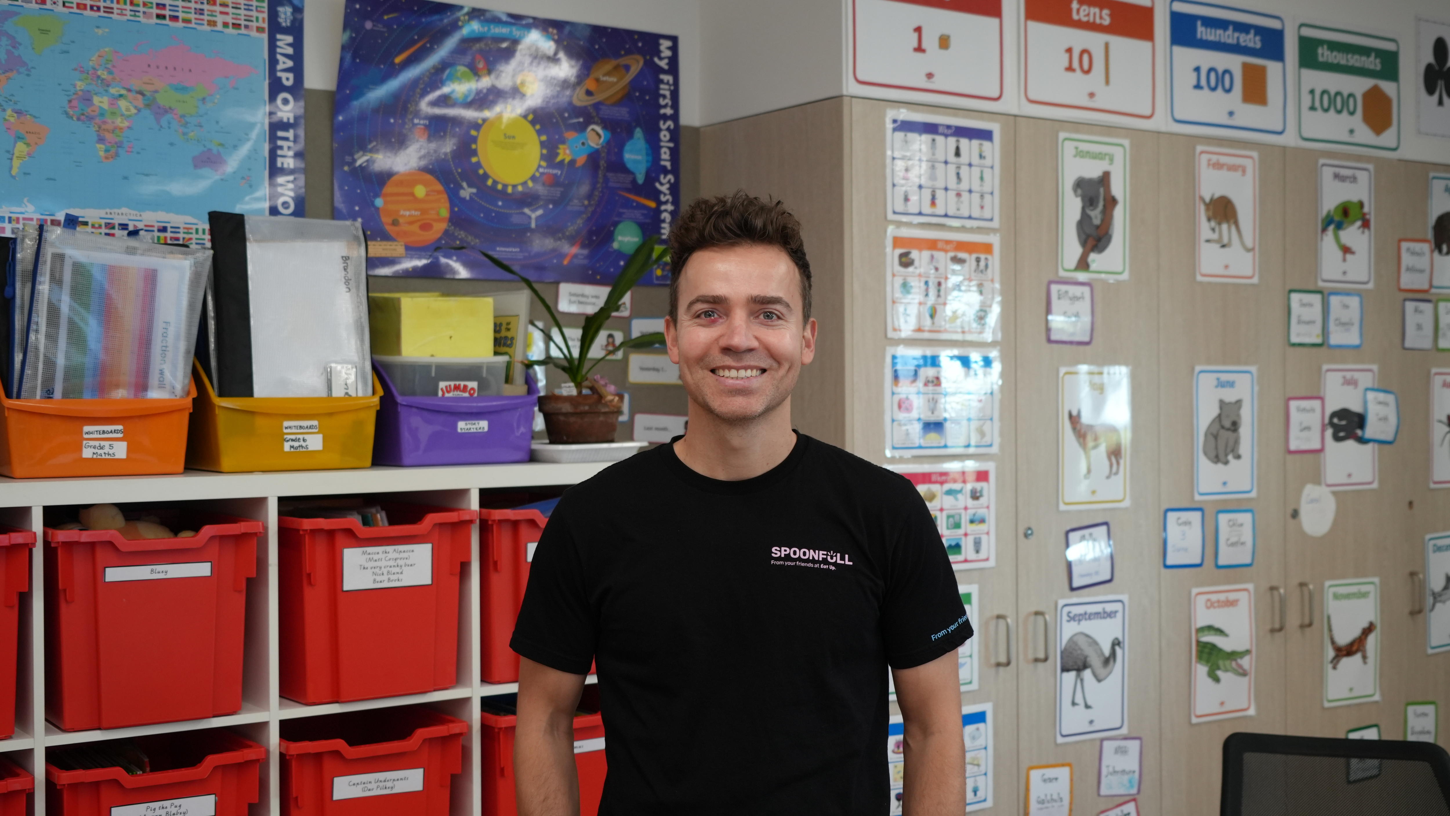 Lydon, a young man with brown hair, wears a black shirt and stands in a classroom.