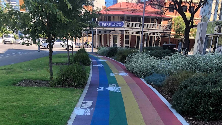 A rainbow coloured path in a city park with white graffiti on it