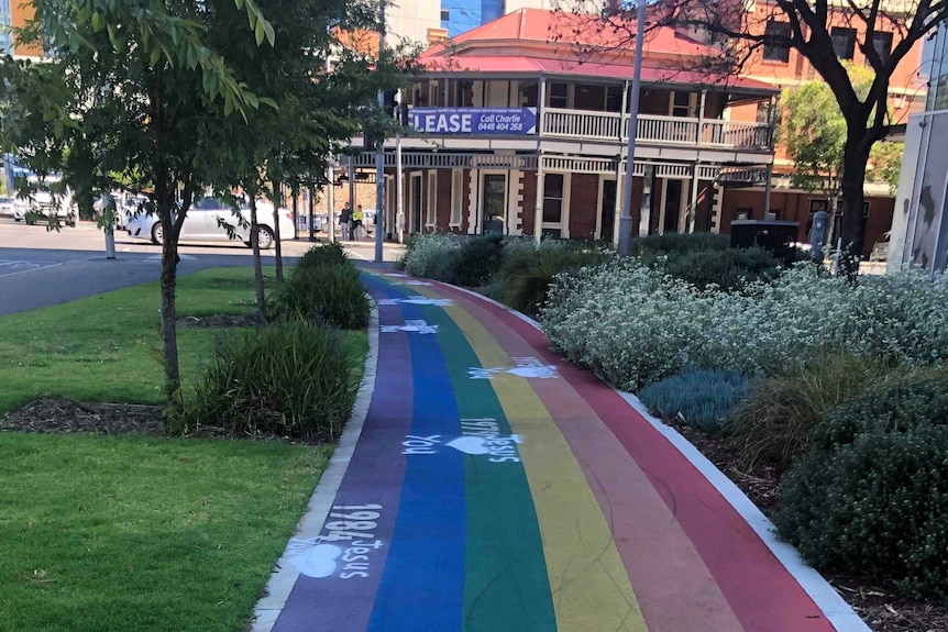 A rainbow coloured path in a city park with white graffiti on it