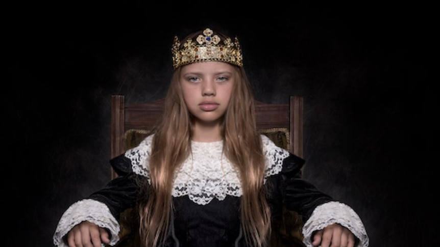 A young Indigenous girl on a throne in black velvet and white lace Shakespearean royal robes with a crown