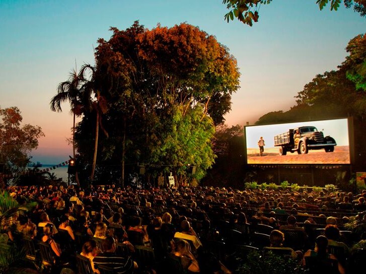 A large crowd watches the screen at outdoor cinema at dusk.