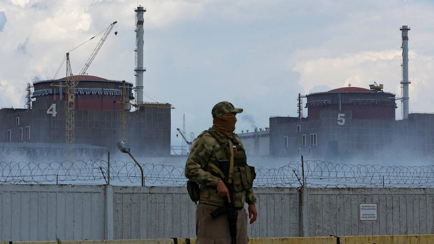 Serviceman stands outside barbed wire fence around nuclear power plant.