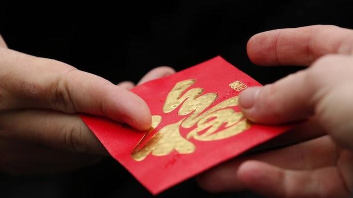 A red envelope is exchanged between hands