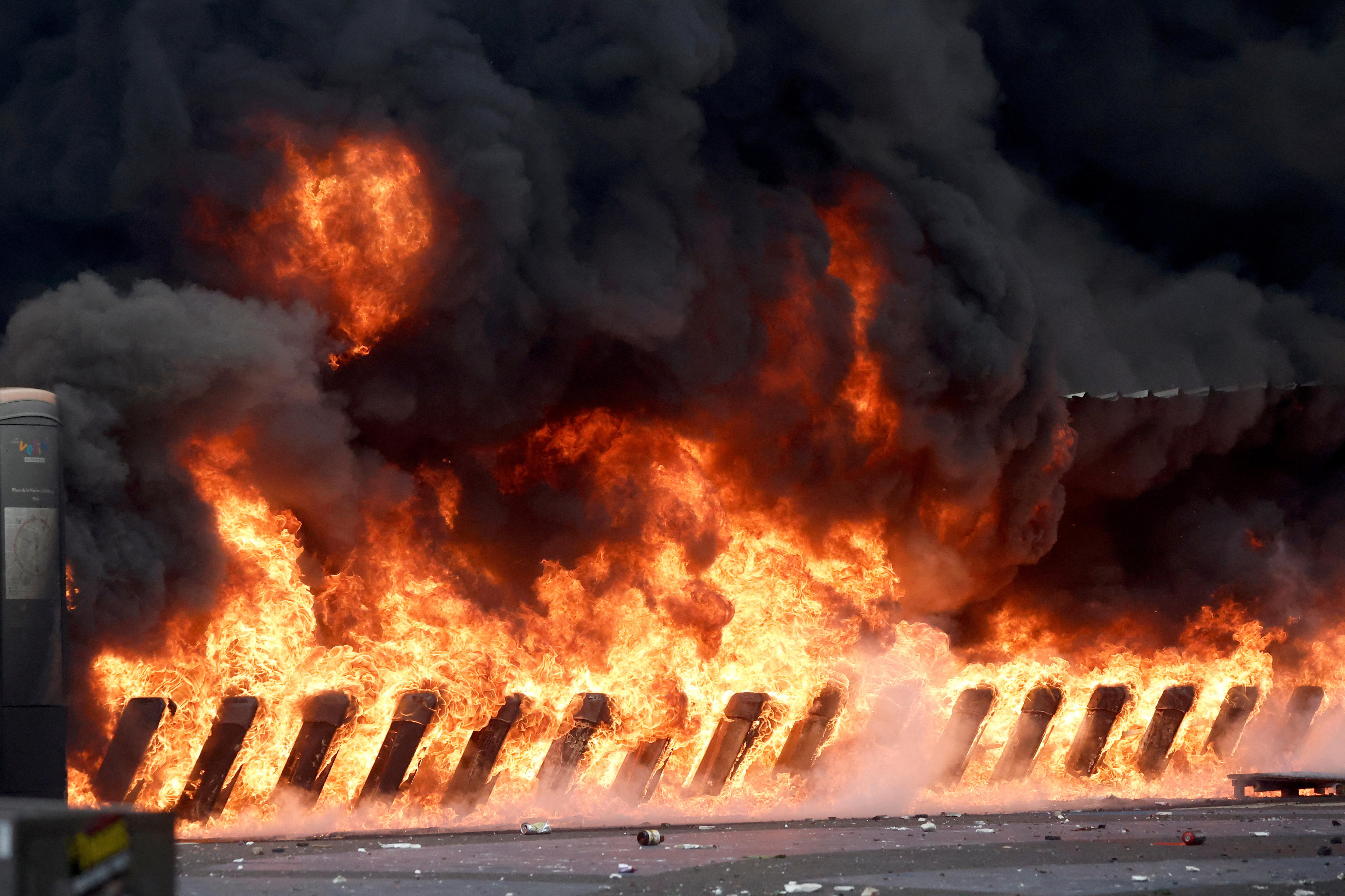 A fence structure is entirely engulfed in flames, fire and smoke on a street in Paris.