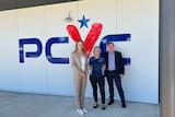 Two women and a man stand side by side in front of a building, with a sign that reads "PCYC".
