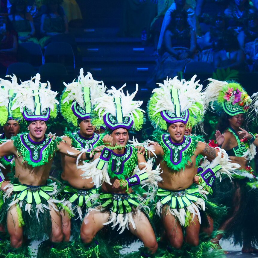 Dancers in bright green, white and blue traditional garb perform onstage.