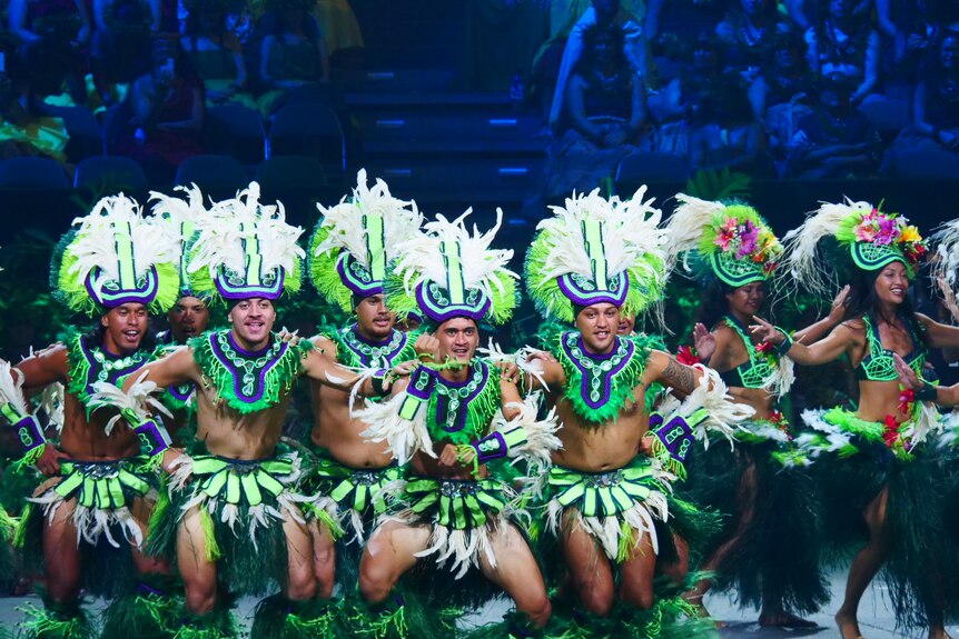 Dancers in bright green, white and blue traditional garb perform onstage.
