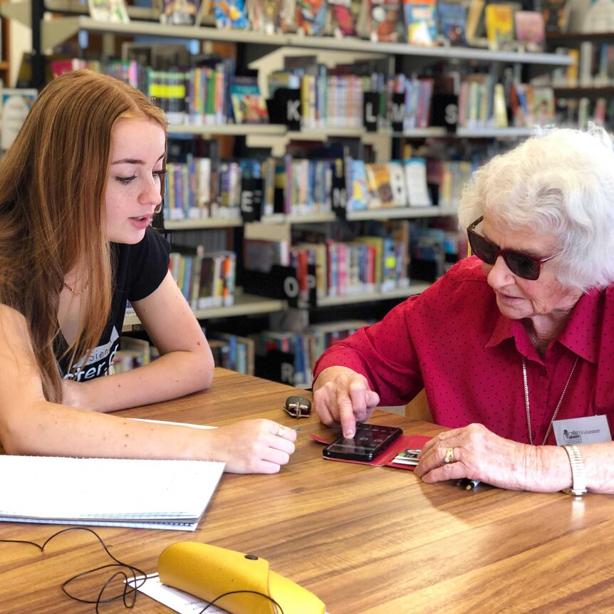 A teenage girl sits with elderly woman Ruth Holmes and teaches her how to use some apps on her phone