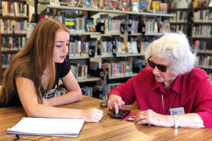 A teenage girl sits with elderly woman Ruth Holmes and teaches her how to use her mobile phone.