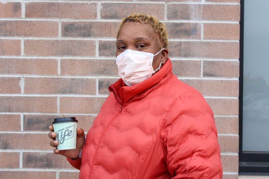 A woman in a red coat and face mask holds a cup which reads 'fuel for life'