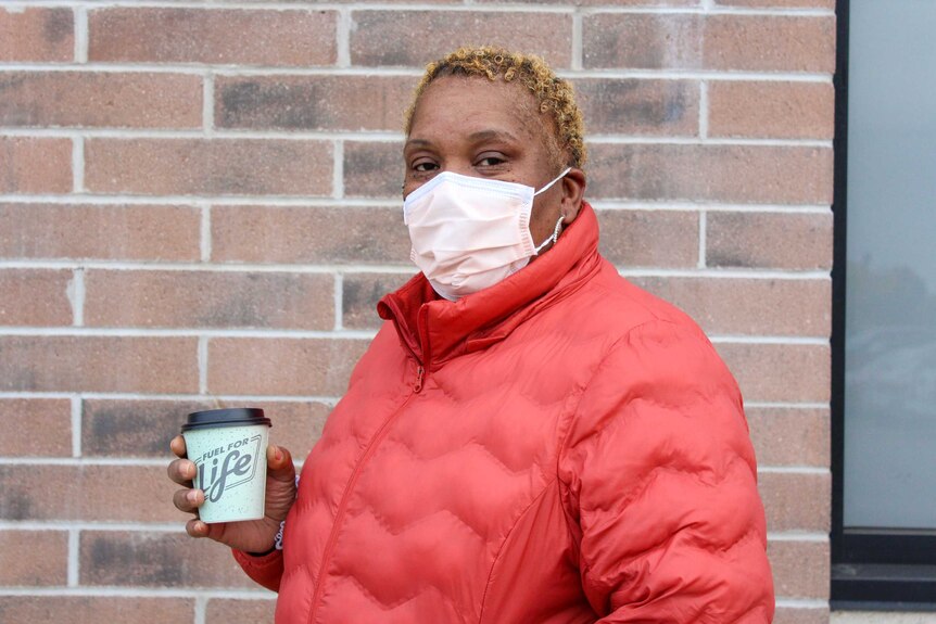 A woman in a red coat and face mask holds a cup which reads 'fuel for life'