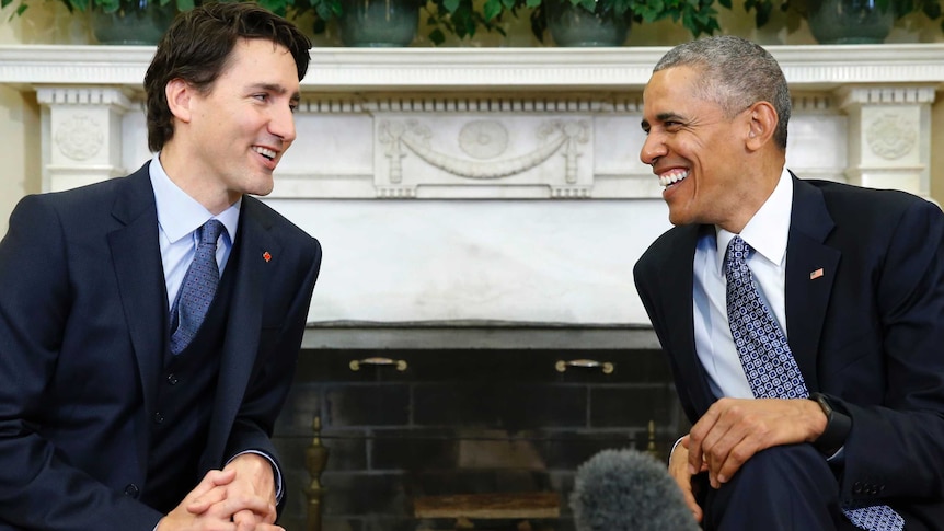 Justin Trudeau and Barack Obama, both seated, look at each other and share a laugh during a meeting in the Oval Office.