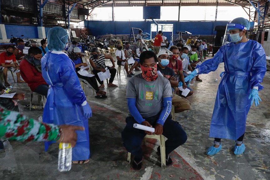 Health workers in protective suits arrange residents during a free COVID-19 swab test in a low income area in Manila.