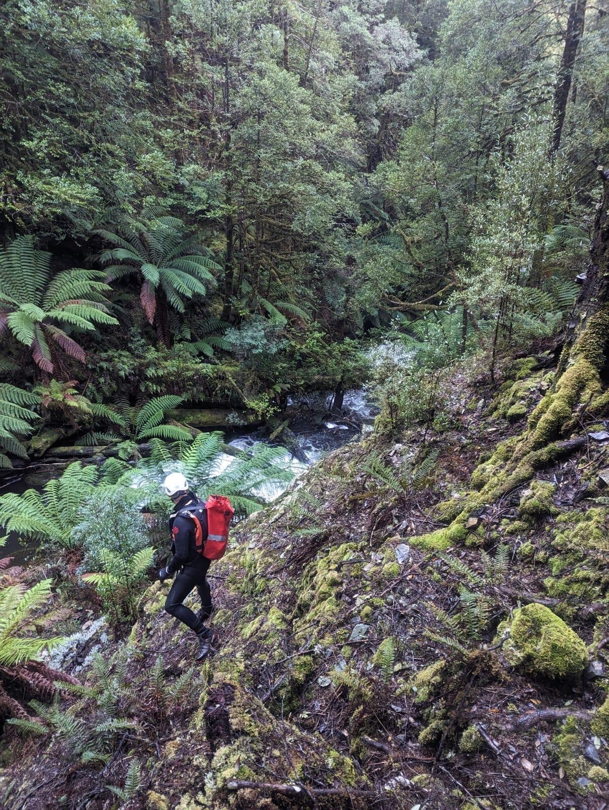 Uma pessoa com capacete e mochila vermelha olha para um rio.