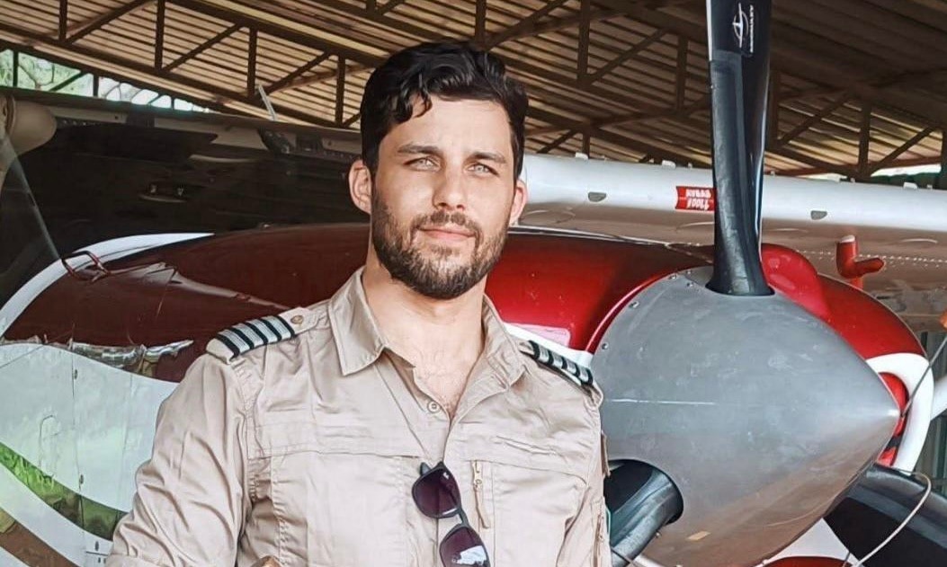 A young man with short brown hair and stubble standing infront of a small plane