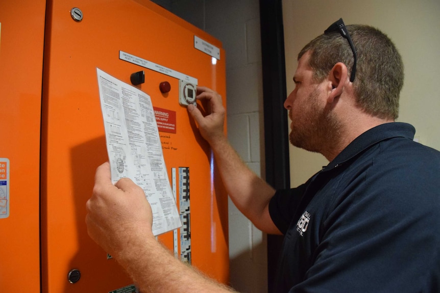 Man hold a sheet of paper and presses buttons on an electrical switchboard