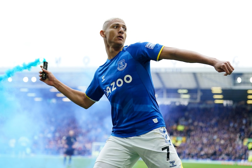 A Premier League player holds a canister emitting light blue coloured smoke as he gets ready to throw it.