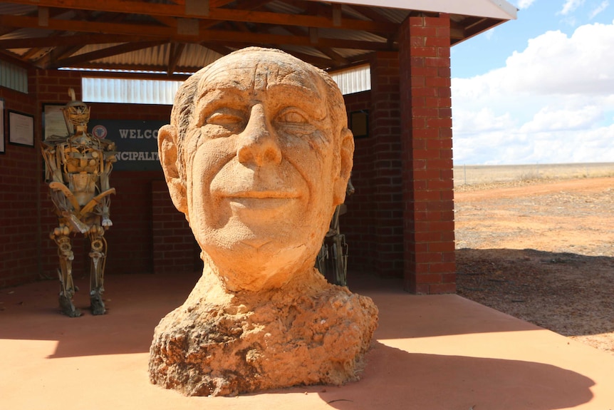 A statue of a man's head in front of a brick shack.